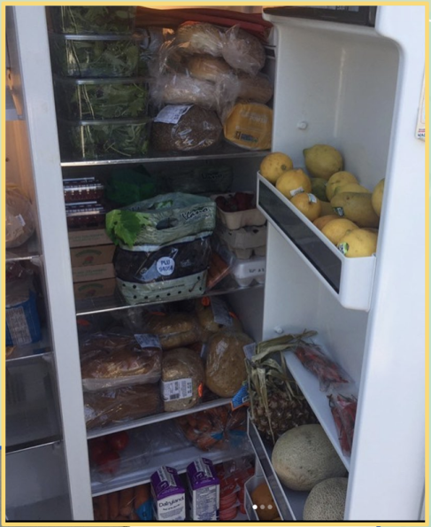 A well-stocked refrigerator containing various items including leafy greens, bread, fruits such as melons and lemons, eggs, and juice cartons.