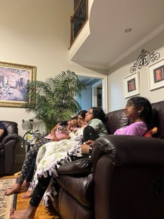 A group of people are relaxing together on a brown leather couch in a cozy living room.