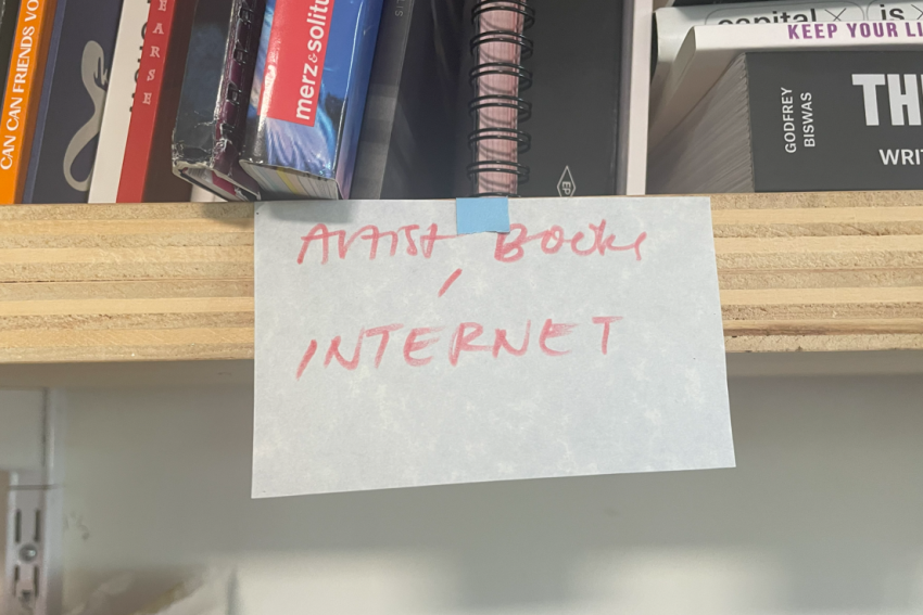 A handwritten note that reads "AVASH BOOK INTERNET" is taped to a wooden shelf filled with books.