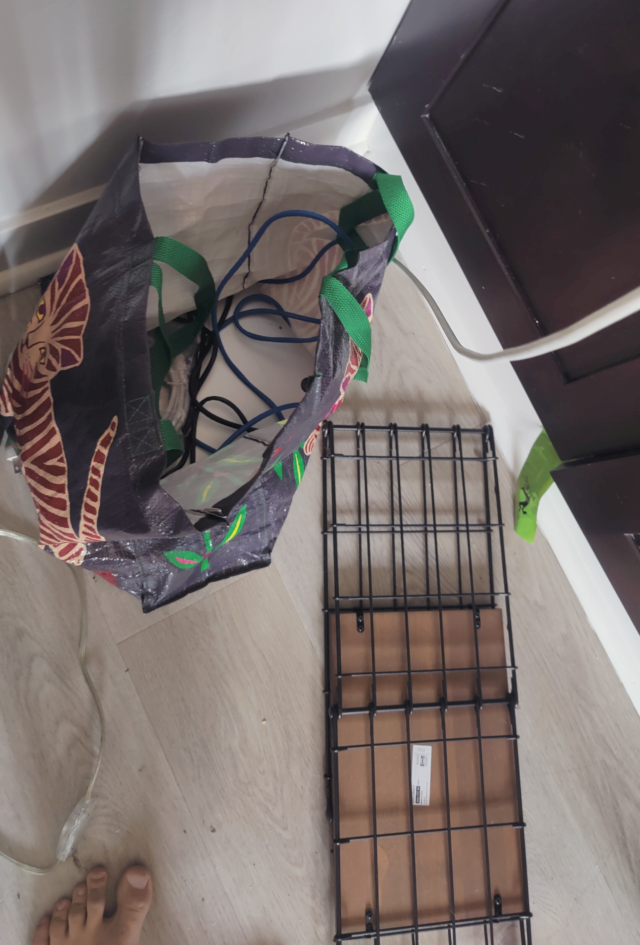 A patterned bag filled with cables sits on a wooden floor next to some wire shelving, and a person's toes are visible at the bottom of the image.