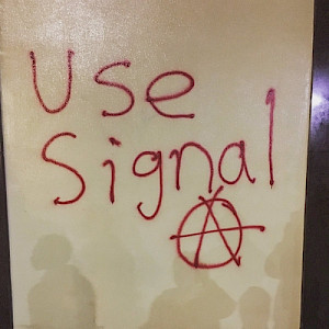 photo of red graffiti on a wall that says "Use Signal" next to the anarchy a symbol